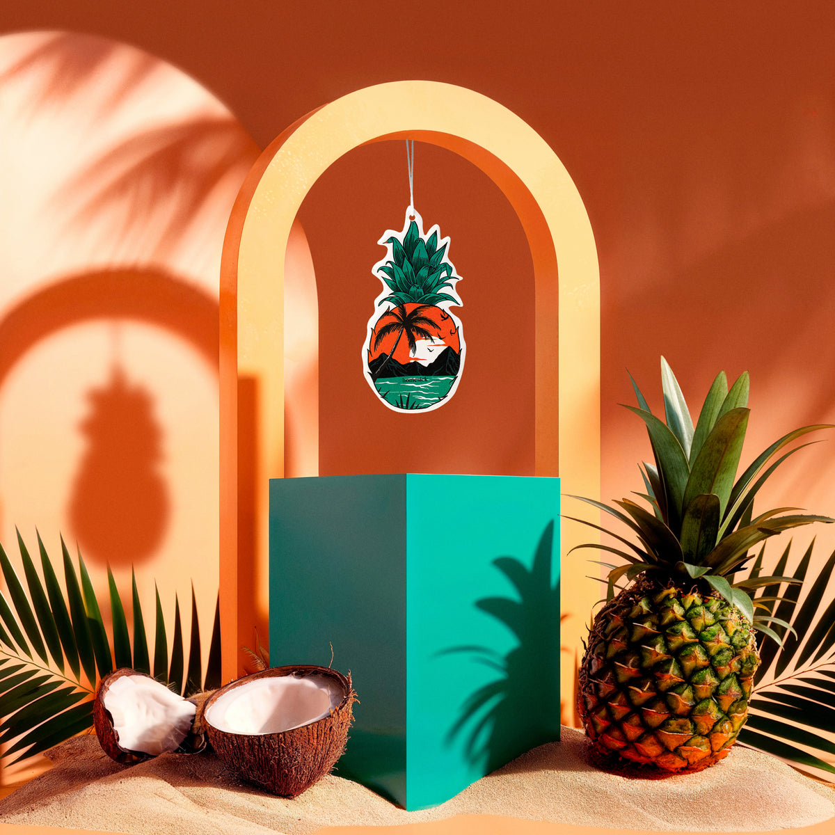 Lifestyle image of a car freshener surrounded by sand and pineapples