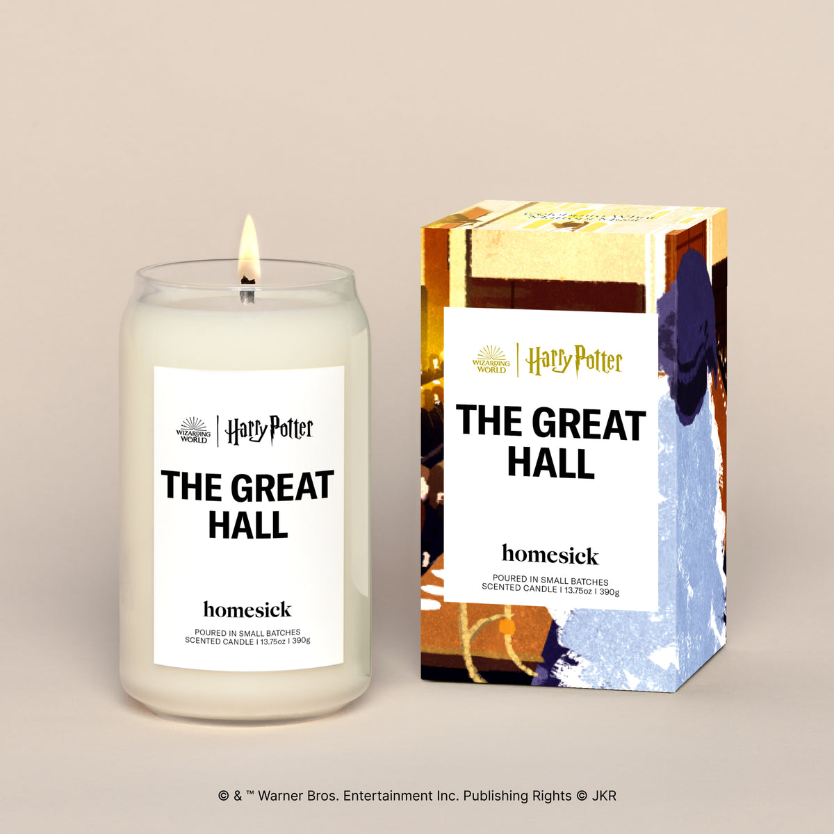 A lit The Great Hall candle displayed next to its boxed packaging on a dark cream background.