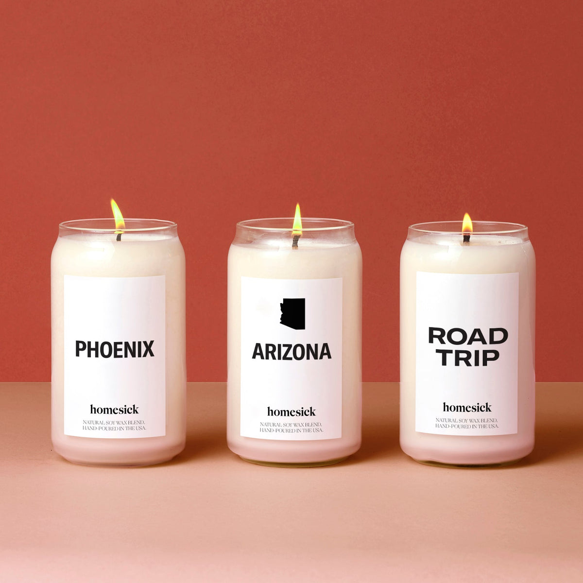 Three Homesick Candles linedup on a salmon table with a warm red background.
