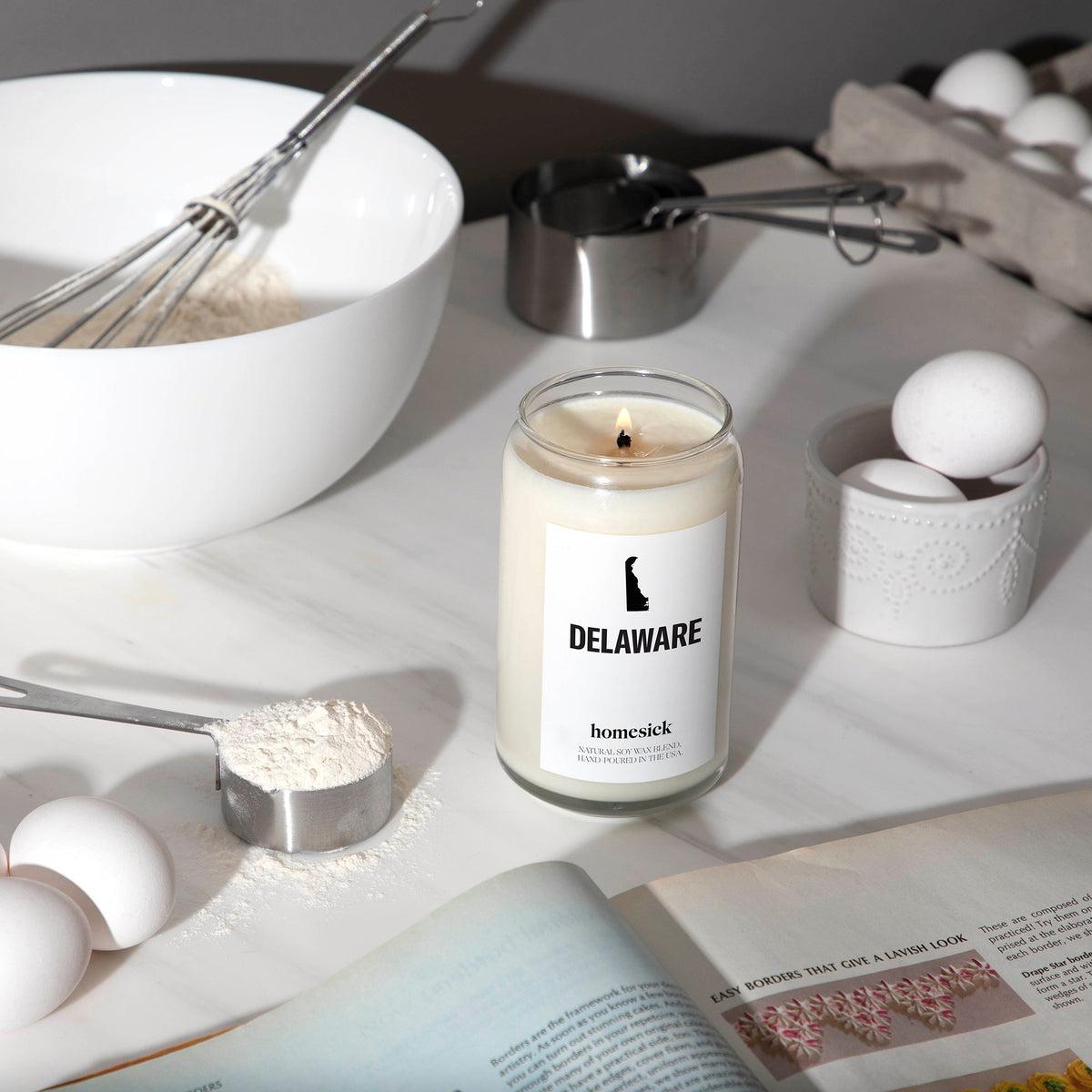 A lit Delaware candle in the middle of a kitchen baking setup.