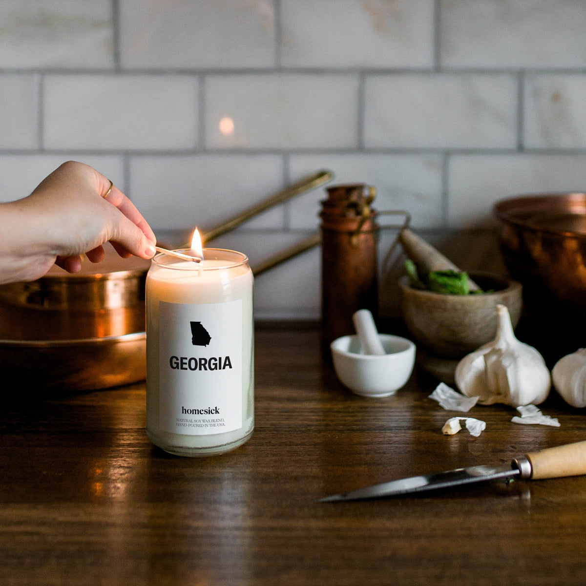 A hand lighting the Georgia candle with a blurred kitchen background.