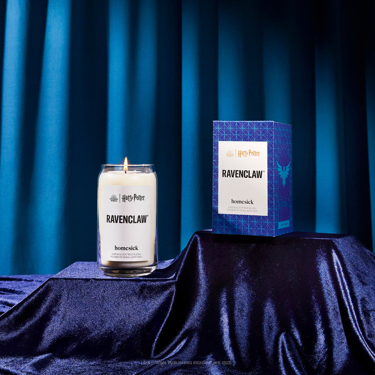 A product shot of the Ravenclaw candle shot on a silky fabric with a blue fabric background.