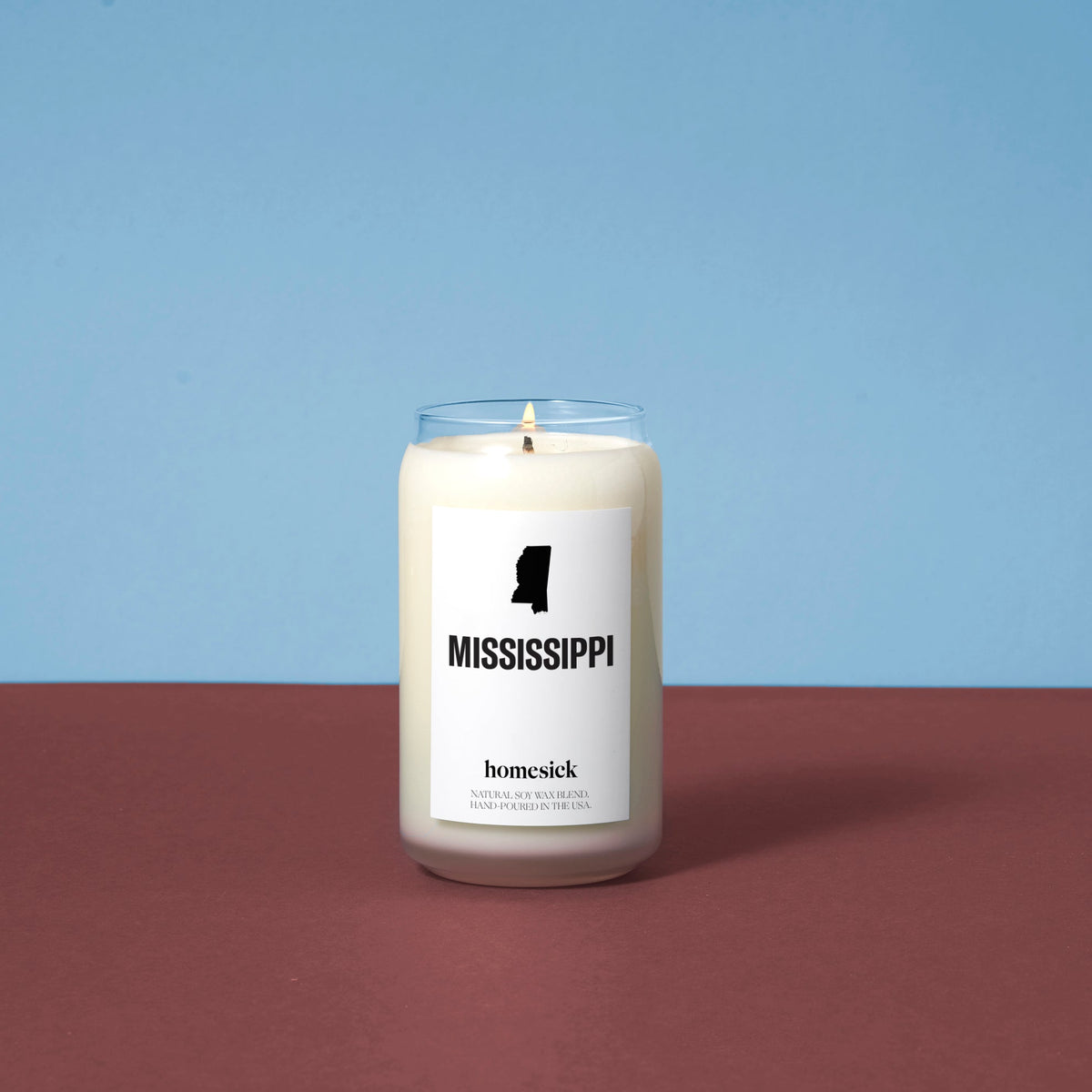 A lit Mississippi Candle on top of a deep amber surface with a blue background.