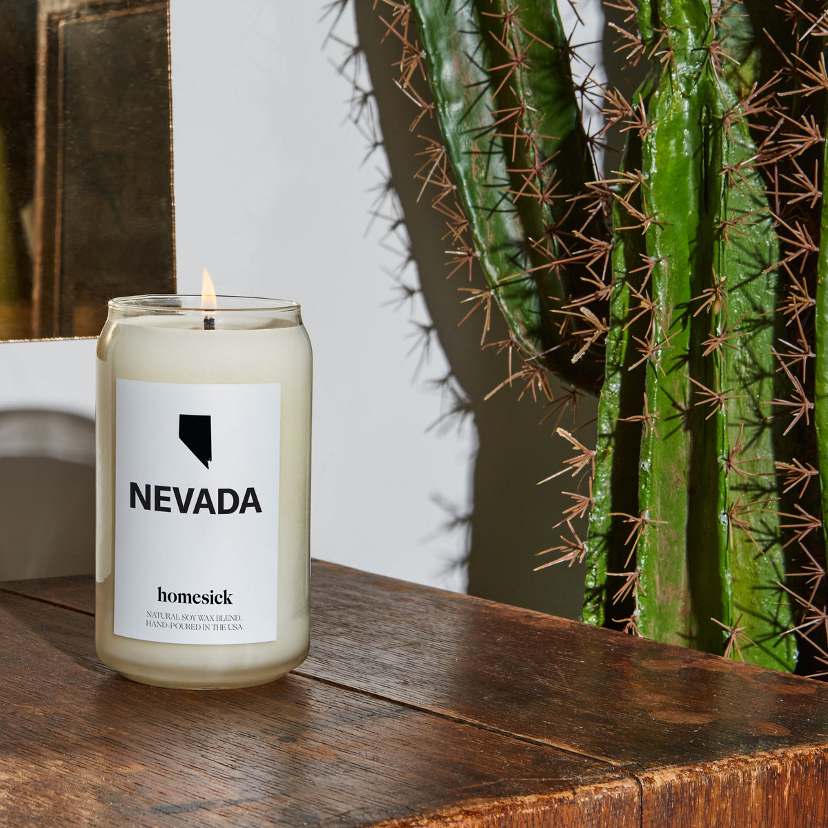 A closeup of the Nevada candle displayed on a dark rustic wood surface with a cactus on the right side.
