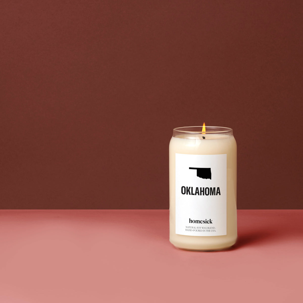A Oklahoma candle on a dark salmon pink surface with a deep ruby red background.