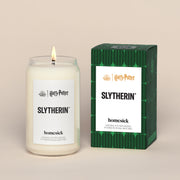 A lit SlytherinHomesick candle displayed next to its boxed packaging on a dark cream background.